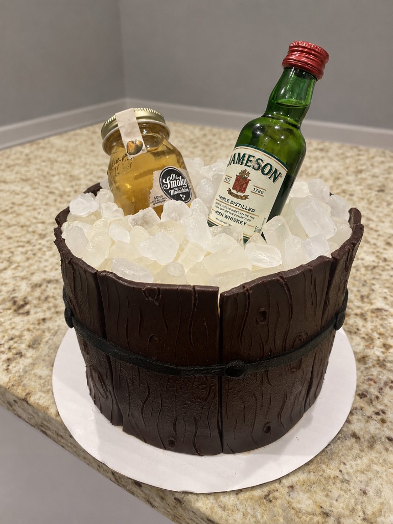 Wooden whiskey-bucket cake with Jameson and moonshine bottles on sugar ice