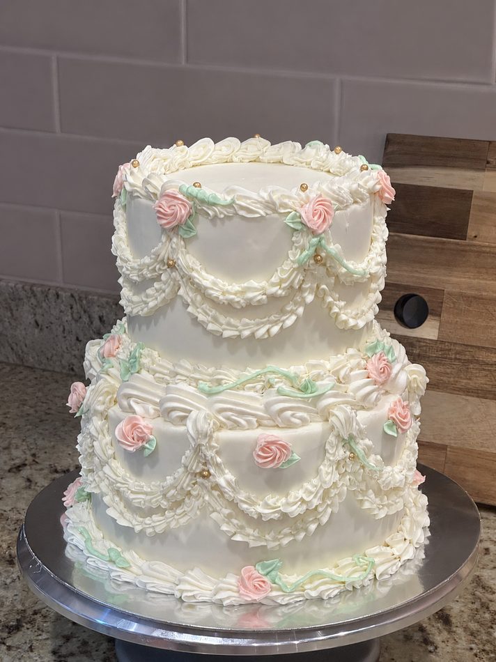 A two-tier vintage buttercream cake with pink roses and gold pearls